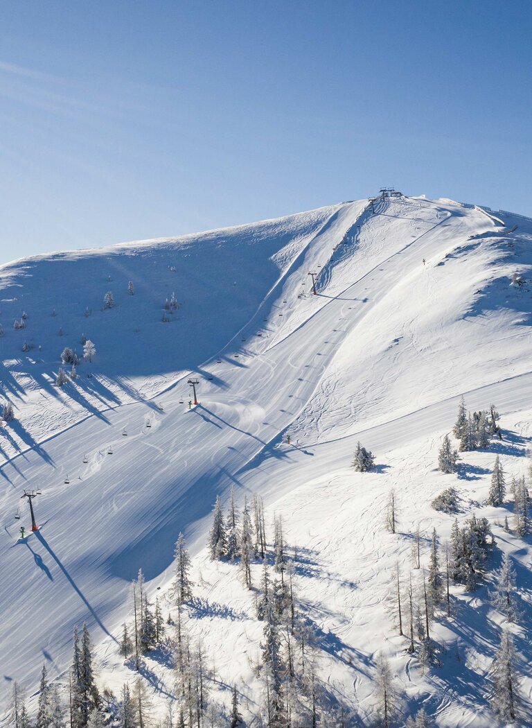 Wide groomed ski slope crosses a snow-covered mountain ridge with ski lifts and scattered trees. | © Galsterbergalm Bahnen GmbH & Co KG 