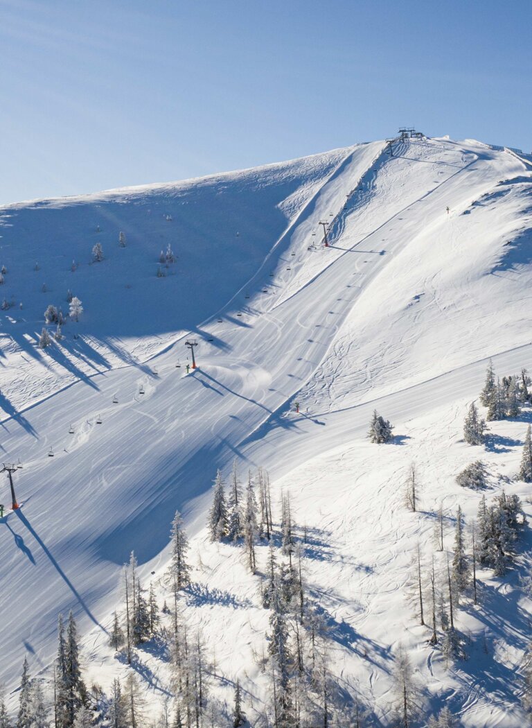 Breite präparierte Skipiste führt über einen verschneiten Bergrücken mit Liftanlagen und verstreuten Bäumen. | © Galsterbergalm Bahnen GmbH & Co KG 