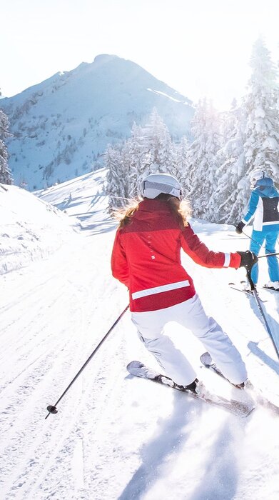 Vier Skifahrer fahren bei Sonnenschein durch eine verschneite Waldpiste mit glitzerndem Schnee und Berglandschaft im Hintergrund. | © Ski amadé GmbH